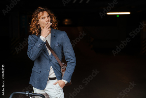 Young ginger long-haired man smoking cigarette outdoors