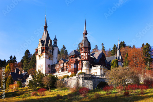 View of Peles castle with arranged courtyard and colorful autumn forest in Sinaia, Romania, Europe
