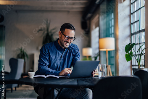 Smiling adult man typing something over the laptop, working online.