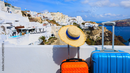 The banner of travel concept with two luggage with hat and landscape view of Oia town in Santorini island in Greece , Greek landscape as blue sky background