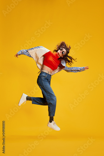 Portrait of young stylish girl posing in casual clothes, jumping, dancing isolated over yellow background