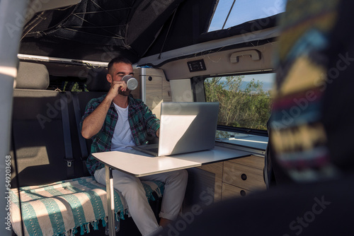 young man working on his laptop from his camper van, concept of freedom and digital nomad lifestyle