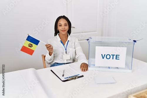 Young african american woman smiling confident holding moldova flag working at electoral college