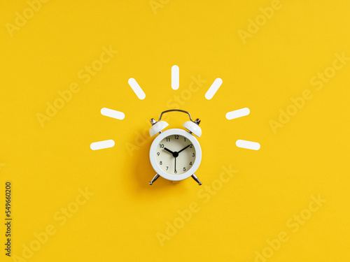 White retro alarm clock ringing on yellow background.