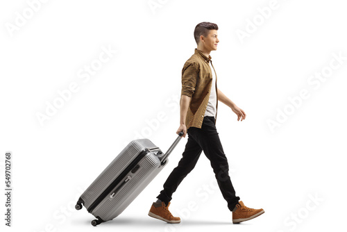 Full length profile shot of a guy walking and pulling a suitcase