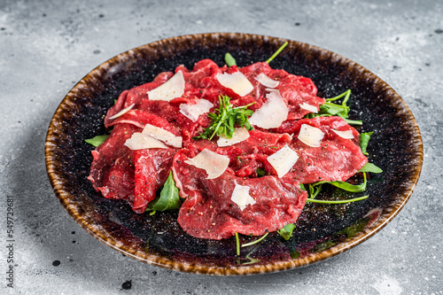 Delicious veal carpaccio with Parmesan cheese, spices and herbs. Gray background. Top view