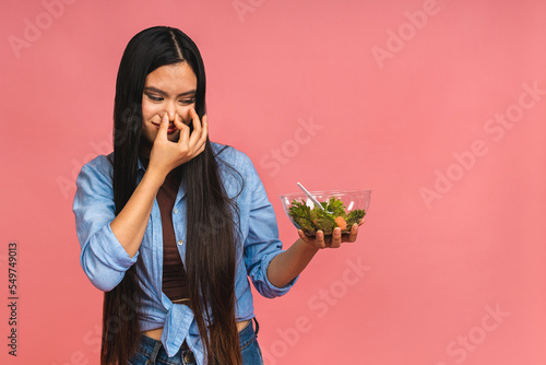 Bad smell of stale food concept. Asian woman holding vegeterian salad or bowl in take away container. Close up, copy space, top view, isolated over pink background.