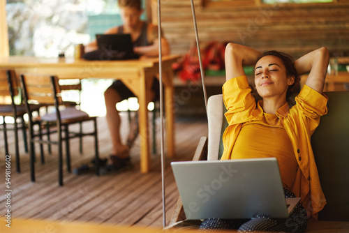 Carefree woman relaxing on swing in cafe shop or coworking hub with her laptop computer. Vacations and sometimes working remotely