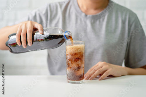 Young woman pouring cold cola soft drink soda from a bottle into a glass in her hand. Health care, healthy diet lifestyle concept.