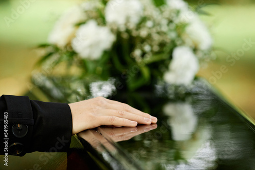 Close up of female hand on coffin saying goodbye at outdoor funeral ceremony, copy space