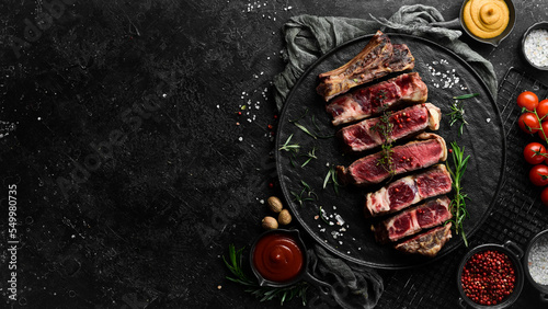 Veal steak on a bone. Juicy pieces of steak. Free space for your text. Top view. On a black stone background.