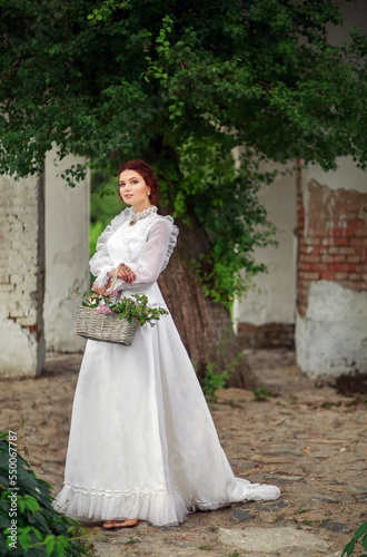 Beautiful girl in a vintage long white dress, and a hairstyle in the English style in a summer park, against the background of columns, warm summer