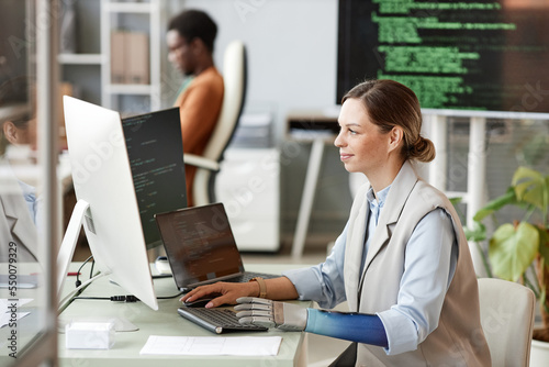 Smiling woman with bionic arm coding on computer when working on big project at research center