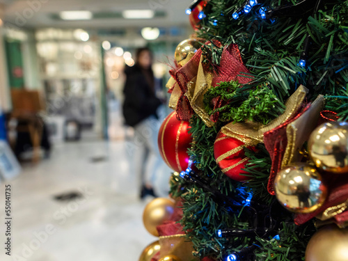 Christmas tree with decorations in focus. Shopping mall with people out of focus in the background.