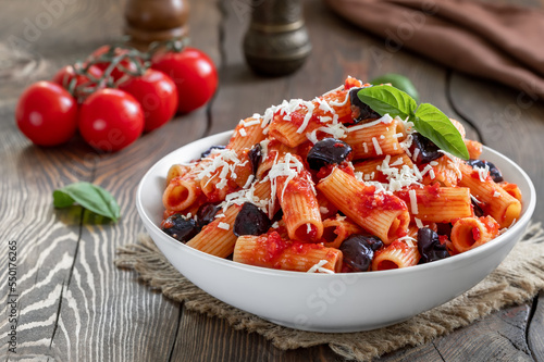 Pasta Alla Norma. Delicious Sicilian pasta dish with roasted eggplant, marinara tomato sauce, grated ricotta and fresh basil served in a white ceramic bowl. Wooden table, selective focus, horizontal.