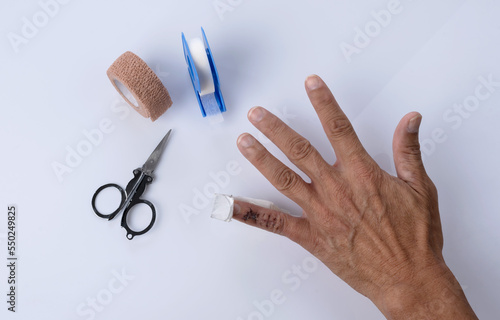 Close up hand with little finger injure and scissors, elastic bandage and tape first aids equipments on white background, Hospital Concept