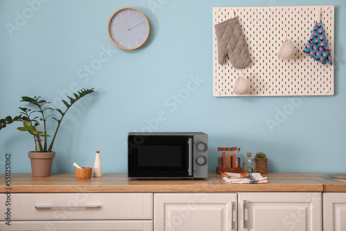 Interior of stylish kitchen with microwave oven near light blue wall
