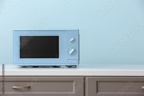 Modern microwave oven on counter near light blue wall