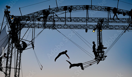 silhouettes of trapeze artists acrobats on the metal scaffolding at sunset