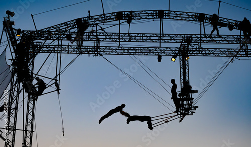 silhouettes of trapeze artists acrobats on the metal scaffolding at sunset