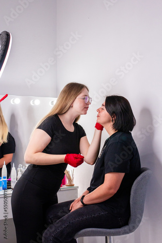Eyebrow master making correction of eye brows of client woman in beauty salon