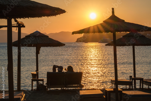 View of a couple lying on sun beds, drinking wine and enjoying the amazing orange sunset in Ios Greece