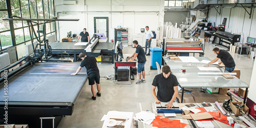 In a large modern printing plant, operators work on various types of machines for printed material