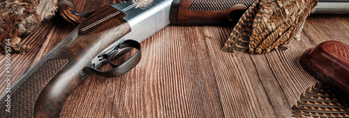 banner concept on the theme of hunting: fragment of a hunting rifle and woodcock plumage on the background of a wooden tabletop, copy space