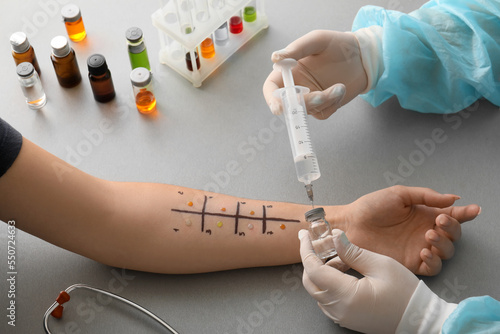 Doctor with syringe and ampule making allergy skin test to patient in clinic, closeup