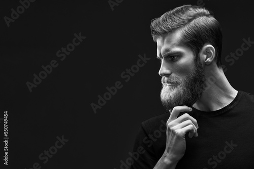 Perfect man's beard. Close-up of young bearded man touching his beard. It's time to shave. Serious handsome old-fashioned hipster in t-shirt. Thinking. Free space on right