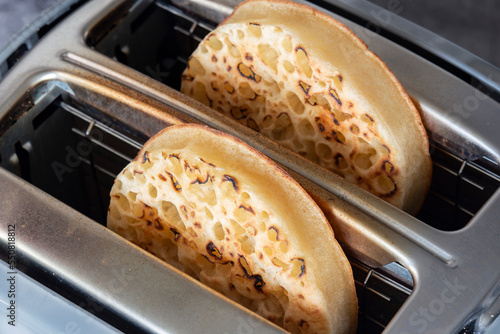 Toasted crumpets cooked in an electric toaster appliance. On a dark stone background