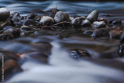tranquil misty stream flowing through smooth natural rocks, pebbles and sticks.