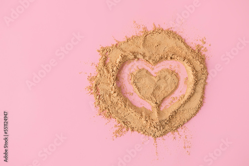 Top view of heart shape made of raw maca root powder on soft pink background with copy space