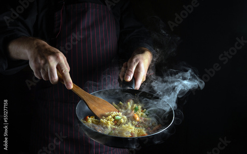 Cooking fresh vegetables and noodles. The chef flips food in a hot frying pan. Space for recipe or menu on black background