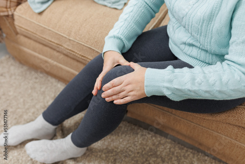 Mature woman suffering from knee ache on sofa