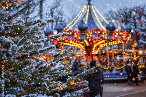 Christmas in Tivoli Gardens, Copenhagen, Denmark, with a snow covered fir tree in front of a defocussed carrousel ride