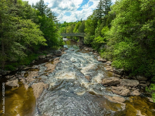 High-angle of blackwater river flowing through stones trees cloudy sunlit sky background