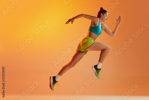 Athlete in motion. Young fitness sportive girl in sports uniform running, training isolated over yellow background in neon light. Dynamic movements, running technique.