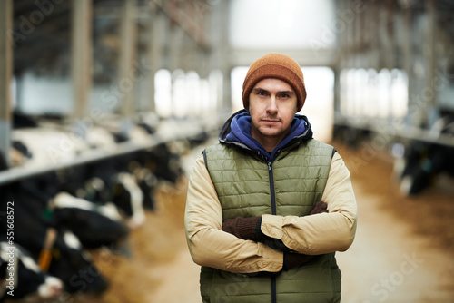 Young serious male owner of large modern livestock farm in waistcoat and beanie cap crossing arms on chest while looking at camera
