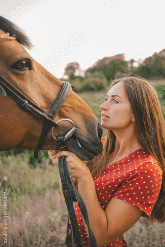 portrait of a beautiful long-haired girl in a red dress and a horse in a grove,