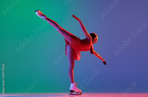 Young sportive girl, junior female figure skater in red stage costume skating isolated over gradient green-blue background in neon light. Grace, beauty, winter sports