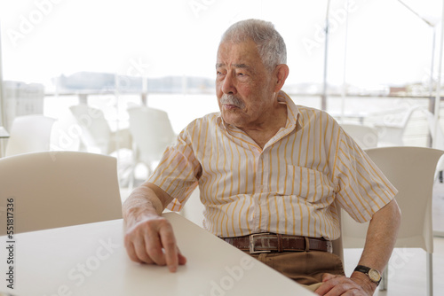  un signore anziano vestitocon camicia seduta al tavolino di un bar