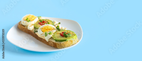 Tasty toast with boiled egg and avocado on light blue background with space for text
