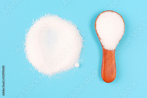 Erythritol powder in a wooden spoon close-up on blue background.