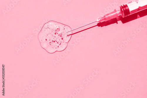 Sterile medical syringe and drop of gelatinous liquid on pink background. Demonstration of colors 2023 Viva Magenta. Flat plan, space for text.