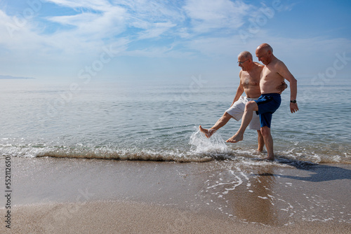 coppia di anziani al mare giocano sula riva schizzando e calciando l''acqua