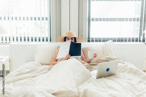 digital nomad and remote working concept - young lady in luxury hotel room bed with hat coffee and laptop