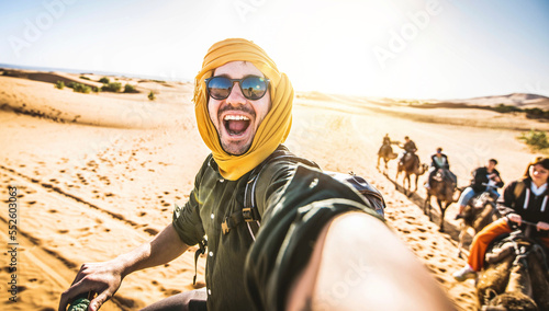 Happy tourist having fun enjoying group camel ride tour in the desert - Travel, vacation activities and adventure concept