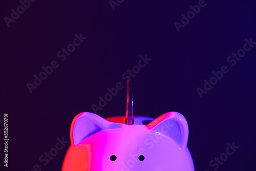 Piggy bank on a dark background with coin and red-purple backlight. Banking concept. Bright neon lights