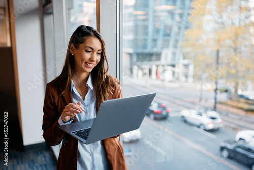 Young happy businesswoman working on laptop by window in office.